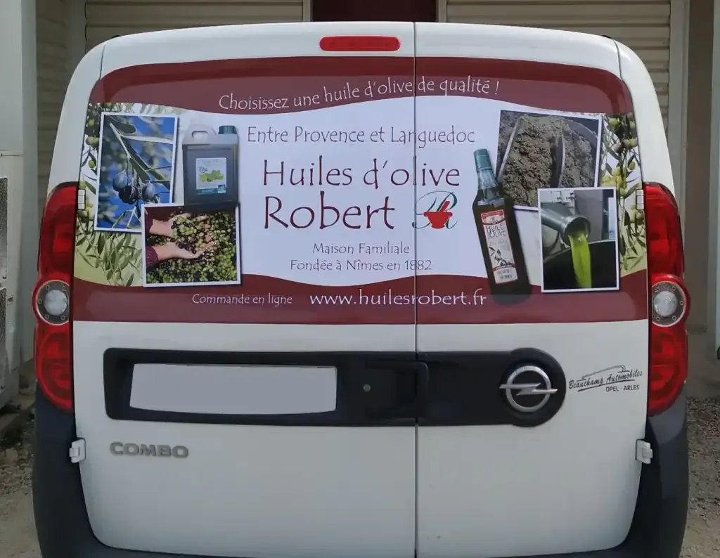 Vue arrière d’un utilitaire blanc recouvert d’un marquage publicitaire pour les Huiles d’olive Robert.