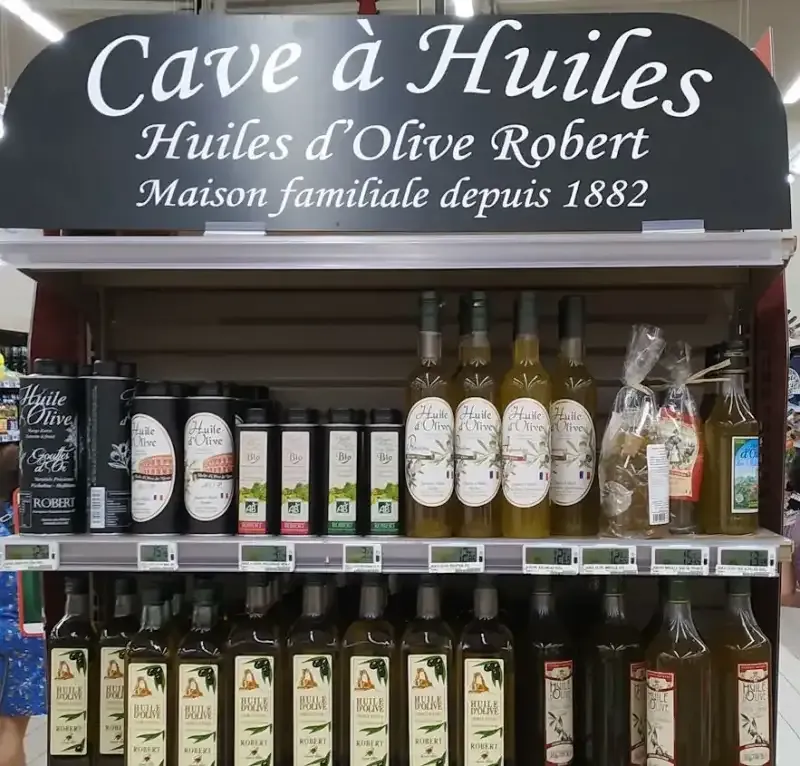 Enseigne noire Cave à Huiles installée au-dessus de bouteilles en rayon.