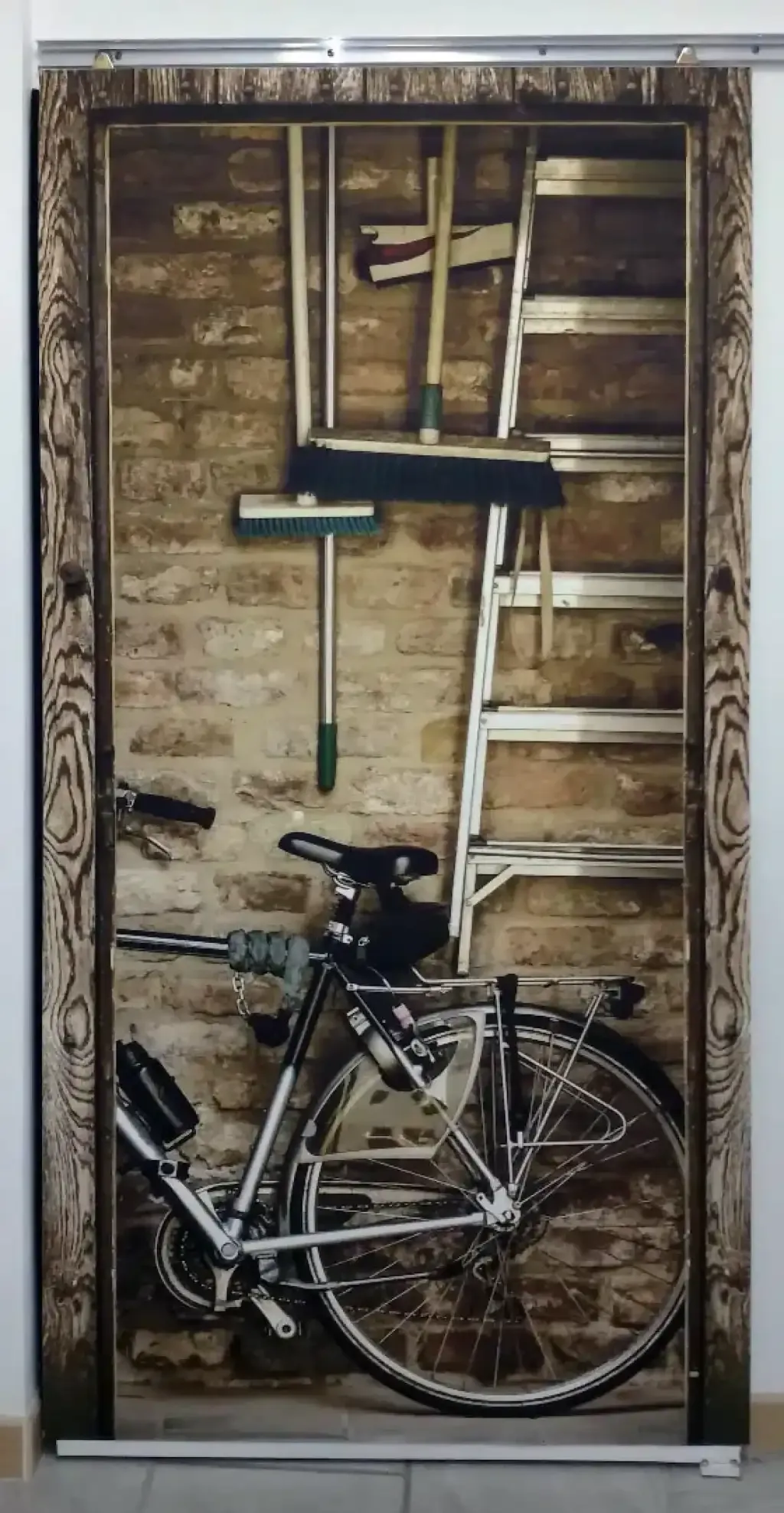 Porte recouverte d’un décor imprimé représentant un vélo et des outils devant un mur en pierre.